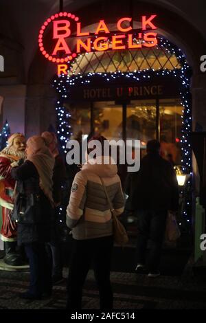 City life - view outside the entrance of a hotel with Pink Black Angels neon bar sign overhead at night in Prague, Czech Republic. December 2019. Stock Photo