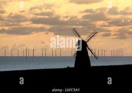 A view of Rottingdean windmill, East Sussex, with the offshore Rampion wind farm in the distance, just before sunset. Old and new forms of wind power. Stock Photo