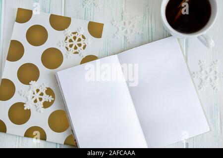 Sample layout of New Year's greetings with snowflakes, open notebook, cup of tea on a light wooden background. Frame for text greetings for Christmas Stock Photo