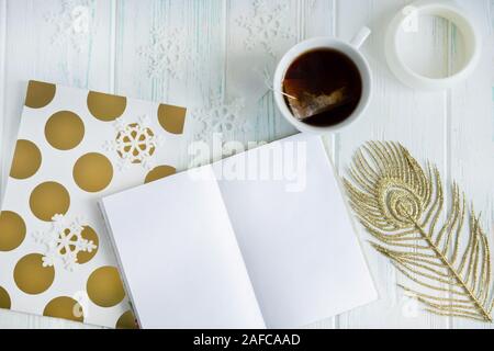 Sample layout of New Year's greetings with snowflakes, open notebook, cup of tea on a light wooden background. Frame for text greetings for Christmas Stock Photo