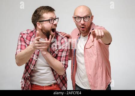 Funny men in glasses point to someone with their hands, they are surprised at what they saw, they are happy and laugh out loud. Stock Photo
