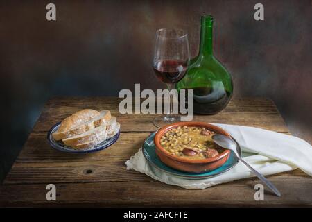 Still life of white beans with wine and bread on an old wooden background, dark food photography Stock Photo