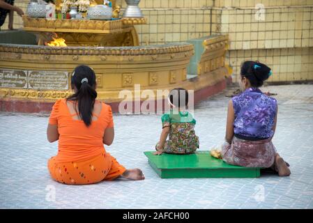Child and women sitting and praying in front of altar, Botahtaung Paya, Buddha's First Sacred Hair Relic Pagoda, Yangon, Myanmar Stock Photo
