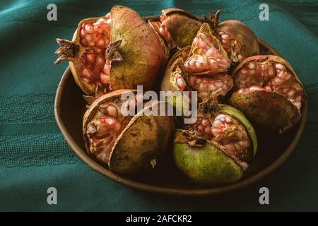 Pomegranates. Cracked pomegranates on a plate close up on green tablecloth on a kitchen table. Vintage, still life Stock Photo