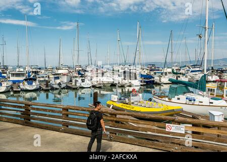 A Chinese tourist looking at a lot of yachts parking in harbor at the Fisherman's Wharf Pier 39 marina in San Francisco, California, United States of Stock Photo