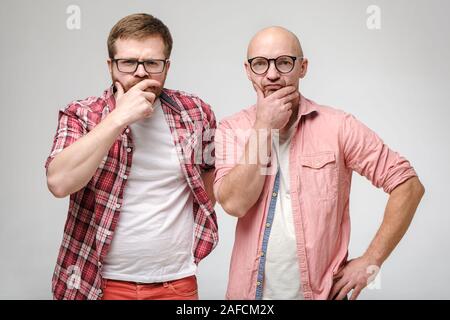 Two serious, pensive men in glasses, hold hands on their faces and stare at the camera in perplexity. Stock Photo