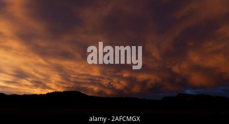 Dramatic yellow and orange light from the setting sun reflected onto storm clouds behind the silhouetted mountains in South Dakota. Stock Photo