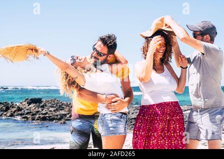 Group of happy adult caucasian people enjoying together the outdoor leisure activity laughing and having fun at the beach with blue beautiful ocean in Stock Photo