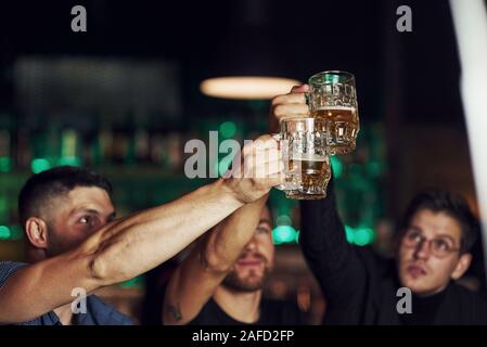 Knocking glasses. Three sports fans in a bar watching soccer. With beer in hands Stock Photo