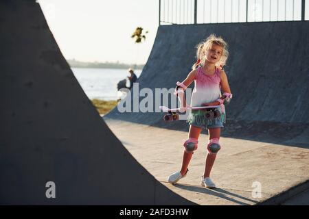 Sunny day. Little girl with scate on a ramp for extreme sports at daytime Stock Photo