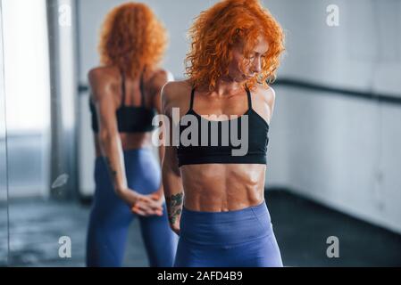 Sporty redhead girl have fitness day in gym at daytime. Muscular body