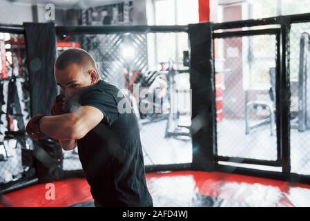 Front view. Young boxer in red bandages have exercise. In the gym on the cage Stock Photo