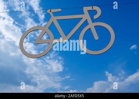 Bicycle lane, grey symbol of a bike hanging from a cable on a blue sky with clouds. Italy Stock Photo