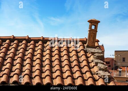 Closeup of a house roof with a terracotta tiles and chimney on a blue sky with clouds. Liguria, Italy, Europe Stock Photo