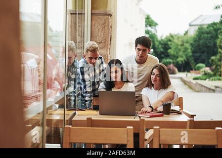 With laptop. Four young students in casual clothes have meeting at rainy day Stock Photo