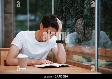 Portrait of young student that sits in cafe at rainy day. One person Stock Photo