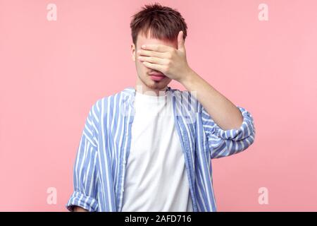 Don't want to watch! Portrait of young serious brown-haired man with small beard in casual striped shirt covering eyes with hand, ashamed or scared. i Stock Photo