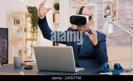 Retired man experiencing virtual reality using vr headset in living room. Cup of coffee on the table. Stock Photo
