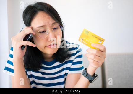 Confused portrait young woman holding credit cards having problem online payment with credit card making rejected unsecure online payment. credit card Stock Photo