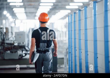 Industrial worker indoors in factory. Young technician with orange hard hat Stock Photo