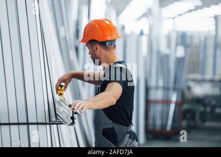 Measuring length of objects. Industrial worker indoors in factory. Young technician with orange hard hat Stock Photo