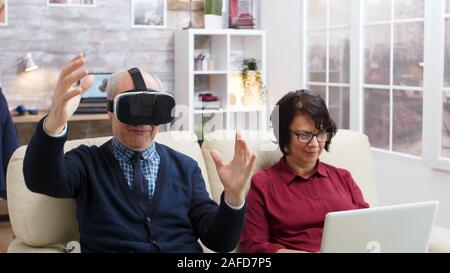 Elderly couple using modern technology to watch movies. Senior with virtual reality goggles. Old lady with laptop. Stock Photo