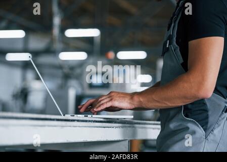 Modern laptop. Typing on keyboard. Industrial worker indoors in factory. Young technician with orange hard hat Stock Photo