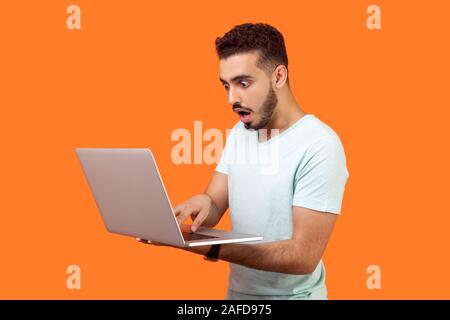 Portrait of young bearded man shocked by message on laptop, having troubles while working on computer program, scared startled face with open mouth an Stock Photo