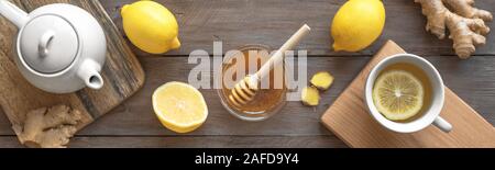 Ginger Lemon Tea with Honey. Warming immune boosting tea with lemon and ginger. Cup, teapot, ginger root on wooden background, top view, banner. Stock Photo