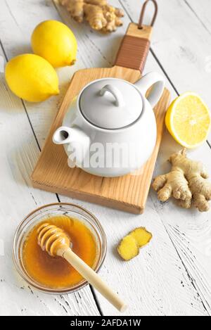 Ginger Lemon Tea with Honey. Warming immune boosting tea with lemon and ginger. Cup, teapot, ginger root on white wooden background. Stock Photo