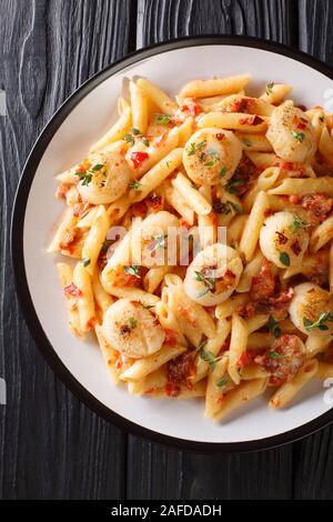 talian penne pasta with scallops, sun-dried tomatoes in a spicy sauce close-up in a plate on the table. Vertical top view from above Stock Photo