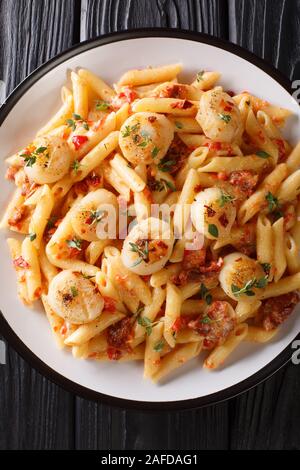 Penne pasta with scallops, tomatoes, herbs and spicy sauce close-up in a plate on the table. Vertical top view from above