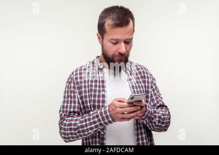 Portrait of concentrated bearded man in casual plaid shirt using smartphone looking serious focused, reading message, email app or surfing the web. in Stock Photo