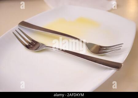 Orange juice on a white empty plate with two forks after eating a fruit salad Stock Photo