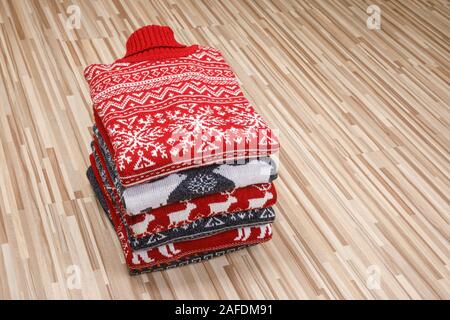 Stack of folded knitted Christmas turtleneck sweaters or pullovers with nordic ornament laid folded on wooden background Stock Photo