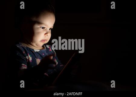 Baby toddler with face lit from phone screen at night, genration z early learning cartoons Stock Photo