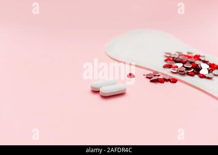 Two pills and menstruation pad with red hearst on it, painkiller contraception medication concept Stock Photo