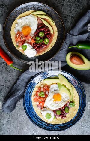Delicious Huevos Rancheros Tostadas, Mexican breakfast consisting of toasted tortilla, chopped tomato and onion, jalapeno and bean mash, topped with f Stock Photo