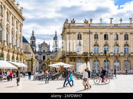 People strolling by the Grand Hotel on the Stanislas square in Nancy, France, closed by a gilded gate with Nancy cathedral in the background. Stock Photo