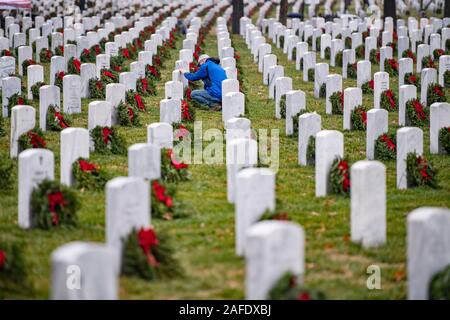 Arlington, United States of America. 14 December, 2019. A man pauses at a gravesite of a fallen service member during the 28th Wreaths Across America Day at Arlington National Cemetery December 14, 2019 in Arlington, Virginia. More than 38,000 volunteers place wreaths at every gravesite at Arlington National Cemetery and other sites around the nation.  Credit: Elizabeth Fraser/DOD/Alamy Live News Stock Photo