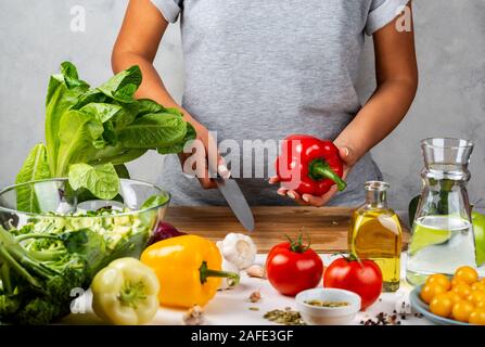 Red pepper and a knife in female hands. Woman is cooking salad. Healthy diet concept. Stock Photo