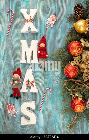 Christmas background. Fir tree branches with Christmas decoration and white wooden letters forming word XMAS on blue background. Stock Photo