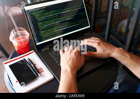 Developer programmer with laptop. Program code and script data on screen. Young freelancer in glasses working on project in cafe. Back view over the Stock Photo