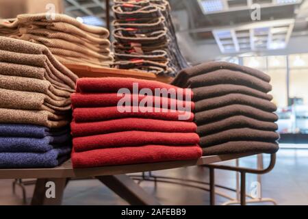 clothes are neatly stacked on the shelves in the store. pullovers, sweaters and warm of different colors are plain. red and other warm shades. close u Stock Photo