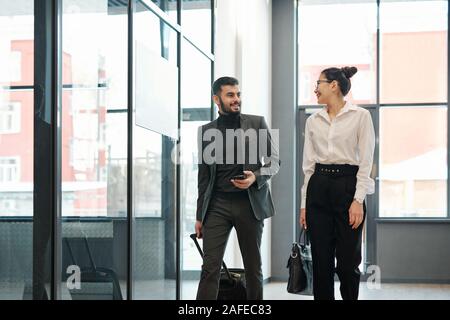 Two young intercultural business colleagues on travel moving along airport Stock Photo