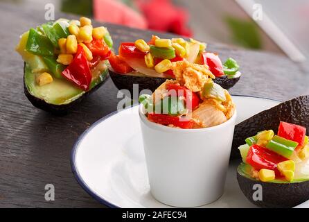 Avocados stuffed with vegetables and scrambled eggs and potatoes on wooden and a light blurred landscape background Stock Photo