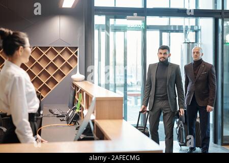 Two elegant business travelers with baggage entering hotel lounge Stock Photo