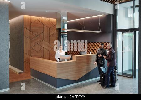Two elegant businessmen with baggage using smartphones in hotel lounge Stock Photo