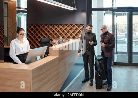 Businessmen discussing data in smartphone while receptionist using computer Stock Photo