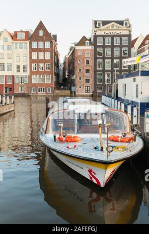 Amsterdam, Netherlands - February 24, 2017: Sightseeing tourist boat moored at the canal in historical center of Amsterdam, vertical photo Stock Photo